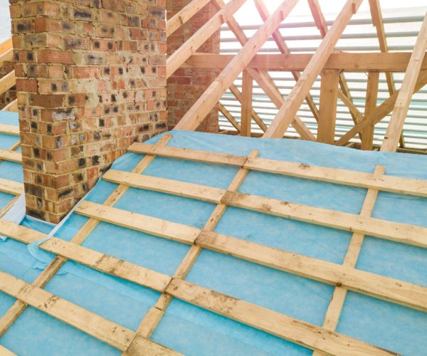 Aerial view of a brick house with wooden roof frame under construction.
