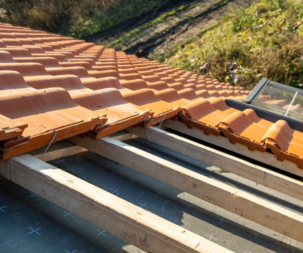 Overlapping rows of yellow ceramic roofing tiles mounted on wooden boards covering residential building roof under construction.