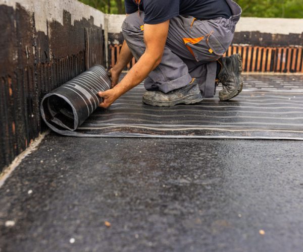 Worker laying the vapor barrier for the roof, bituminous membrane to be welded with flame